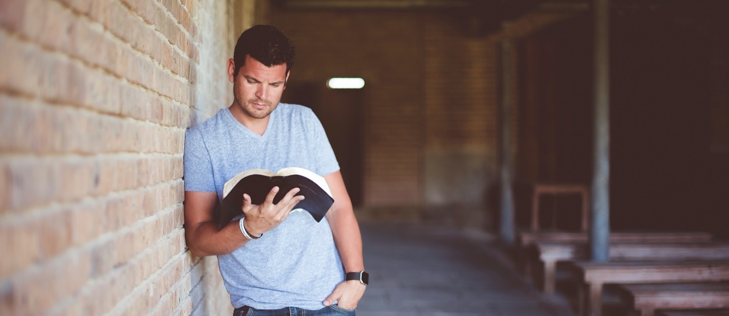 Man leaning against wall reading Bible