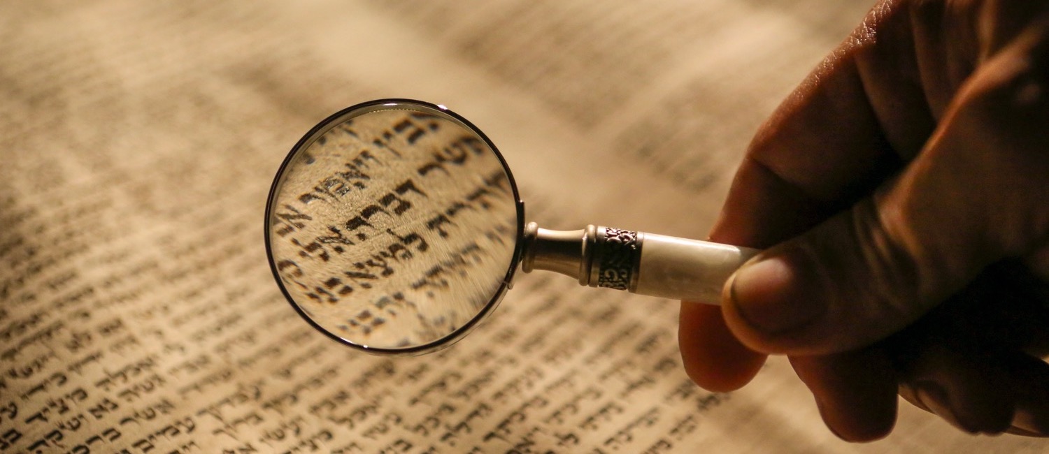 Person holding magnifying glass over Hebrew text